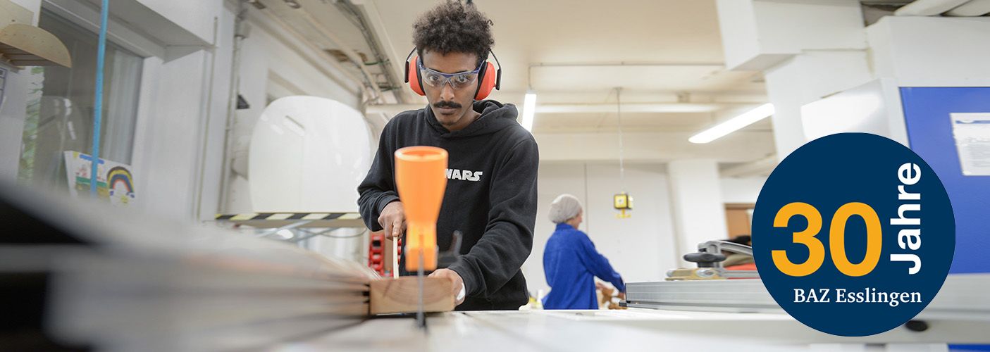 Eine junge Person mit Ohrschützern steht an einer Maschine und bearbeitet Holz.